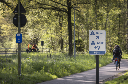 Een routebord toont dat de F70-fietser een rotonde nadert, waar de fietser zijn route naar Bilzen via de F70 of naar Genk via de F701 kan voortzetten.